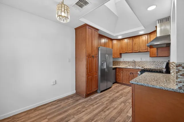 a kitchen with stainless steel appliances granite countertop a refrigerator a sink dishwasher a stove with wooden cabinets and floor