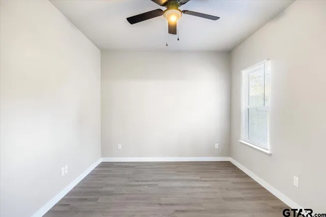 an empty room with wooden floor chandelier fan and windows