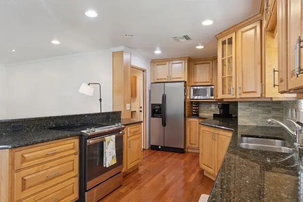 a kitchen with granite countertop a refrigerator a sink a stove and wooden cabinets