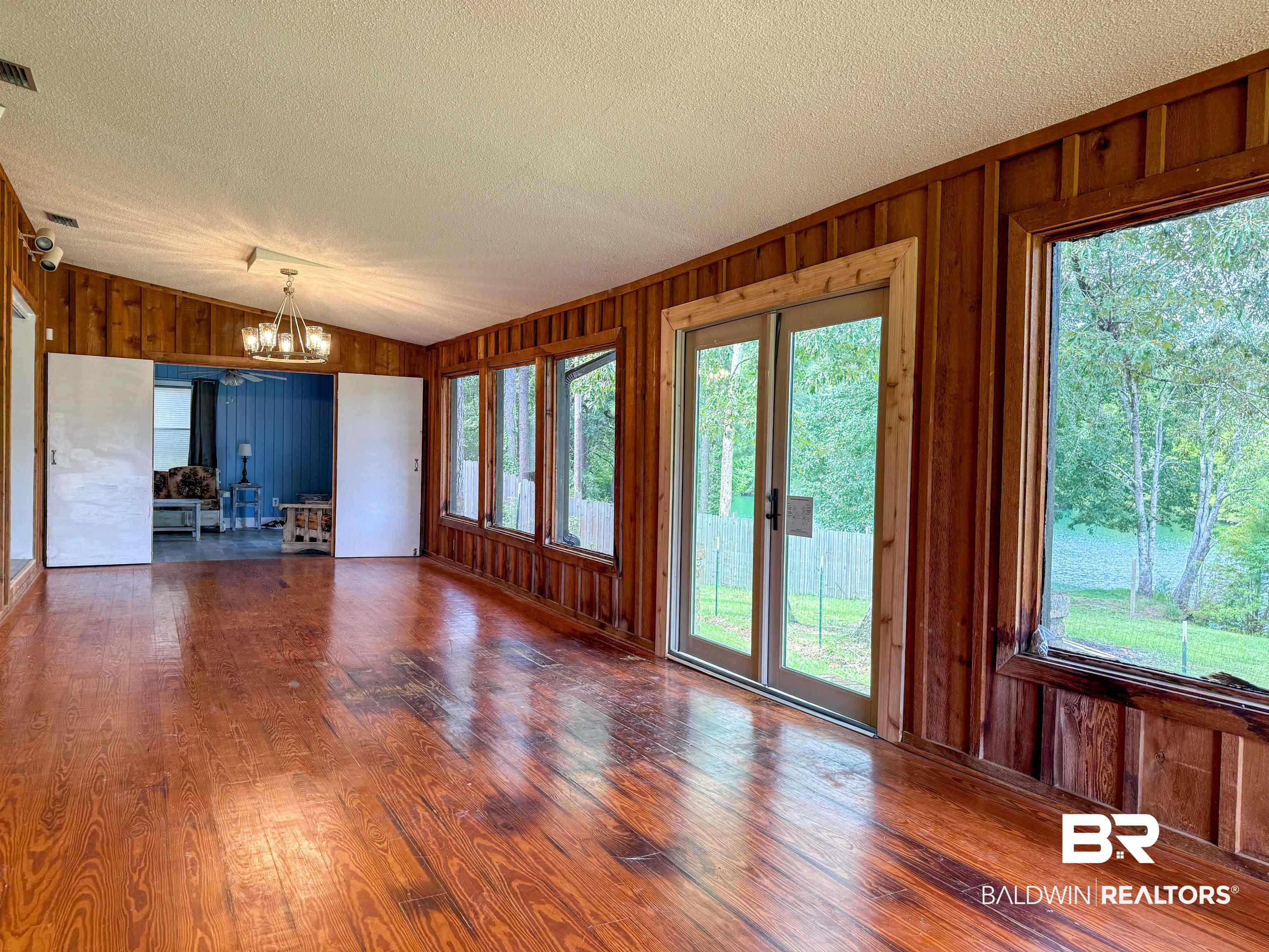 534 Buddy Lake Road Brewton, AL 36426 - Photo 11 of 32 Unfurnished living room featuring wood walls, wood-type flooring, lofted ceiling, a chandelier, and a textured ceiling