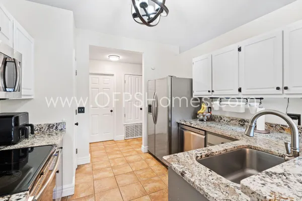 a kitchen with stainless steel appliances kitchen island granite countertop a refrigerator a sink a stove and white cabinets