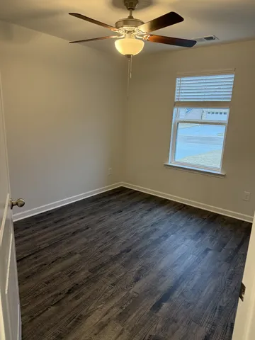 an empty room with wooden floor fan and windows