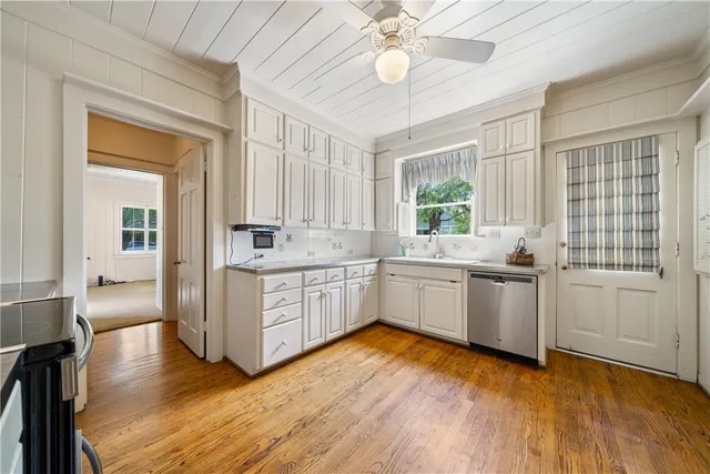 a kitchen with stainless steel appliances granite countertop a stove a sink and white cabinets with wooden floors