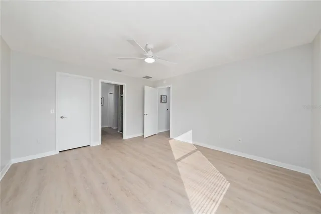 a view of an empty room with wooden floor and a ceiling fan