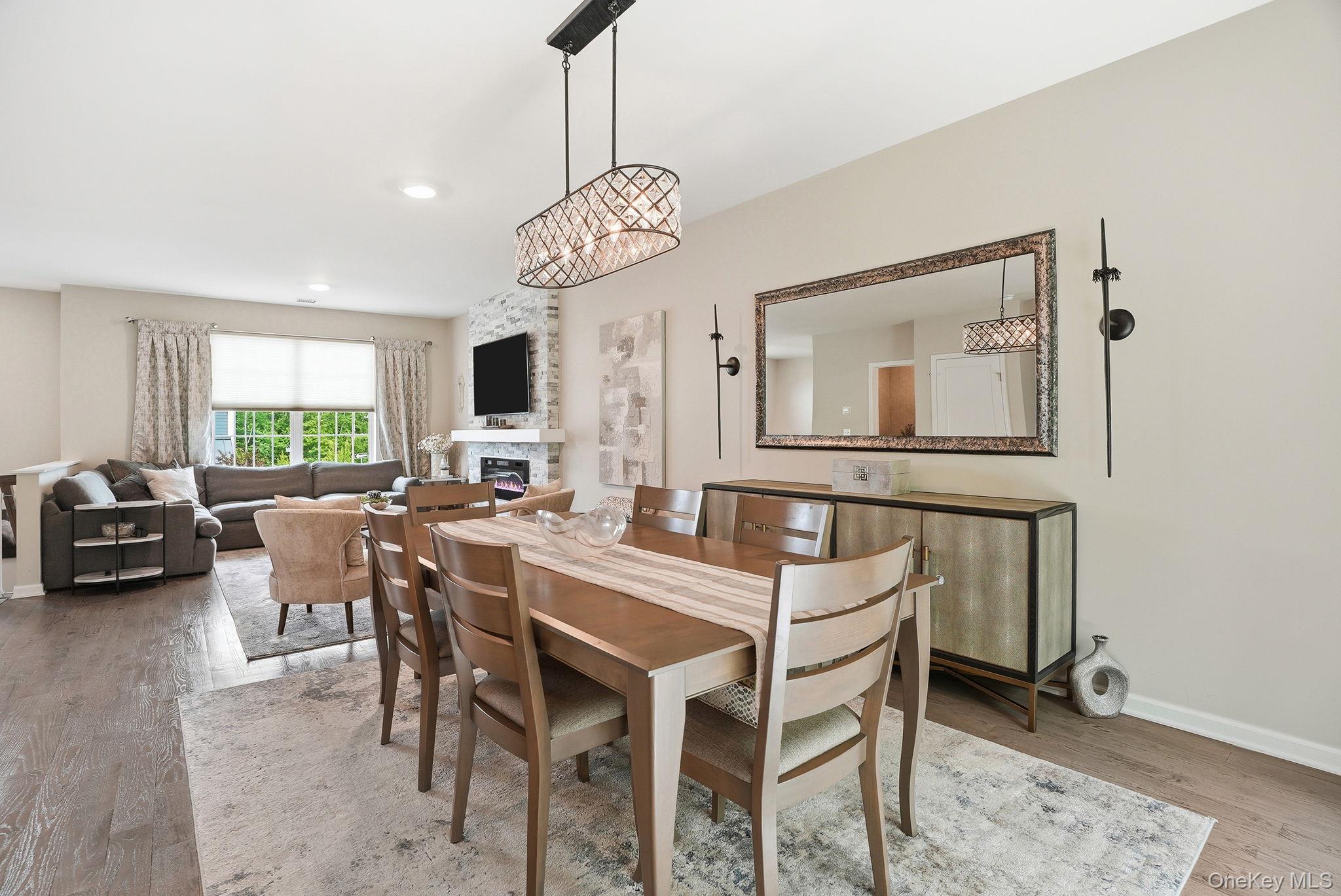 8 Muscoot River Road Granite Springs, NY 10527 - Photo 10 of 40 Open-concept living and dining areas featuring wood-finish flooring, a contemporary chandelier, a built-in stone-clad fireplace, and multiple windows providing natural illumination