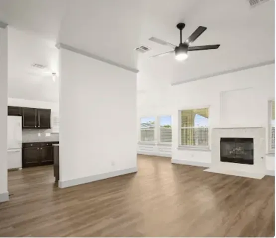 a view of a livingroom with a fireplace a ceiling fan and wooden floor