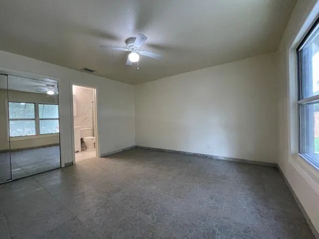 an empty room with chandelier fan and windows