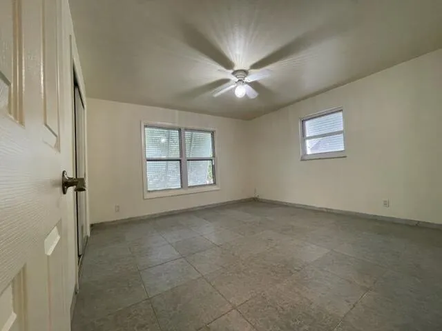 an empty room with chandelier fan and windows