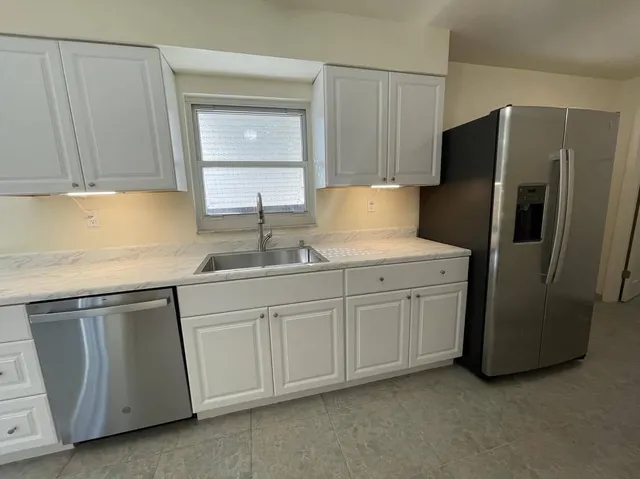 a kitchen with stainless steel appliances granite countertop a refrigerator a sink and white cabinets