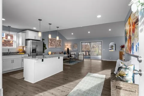 a kitchen with stainless steel appliances kitchen island granite countertop a refrigerator a stove top oven a sink dishwasher and white cabinets with wooden floor