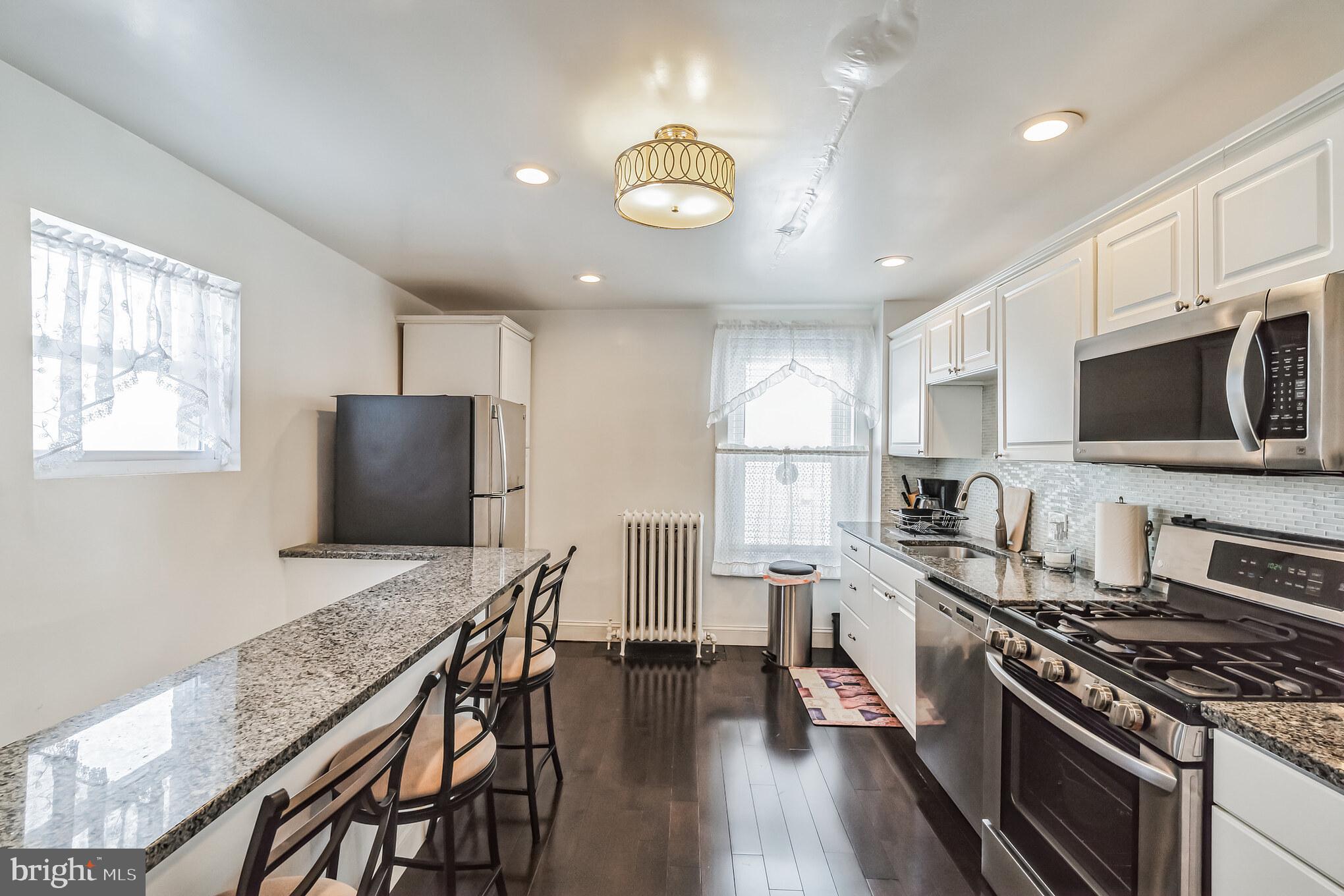 6774 Ridge Avenue, Unit 2 Philadelphia, PA 19128 - Photo 2 of 15 a kitchen with stainless steel appliances granite countertop a stove top oven a sink dishwasher a dining table and chairs with wooden floor