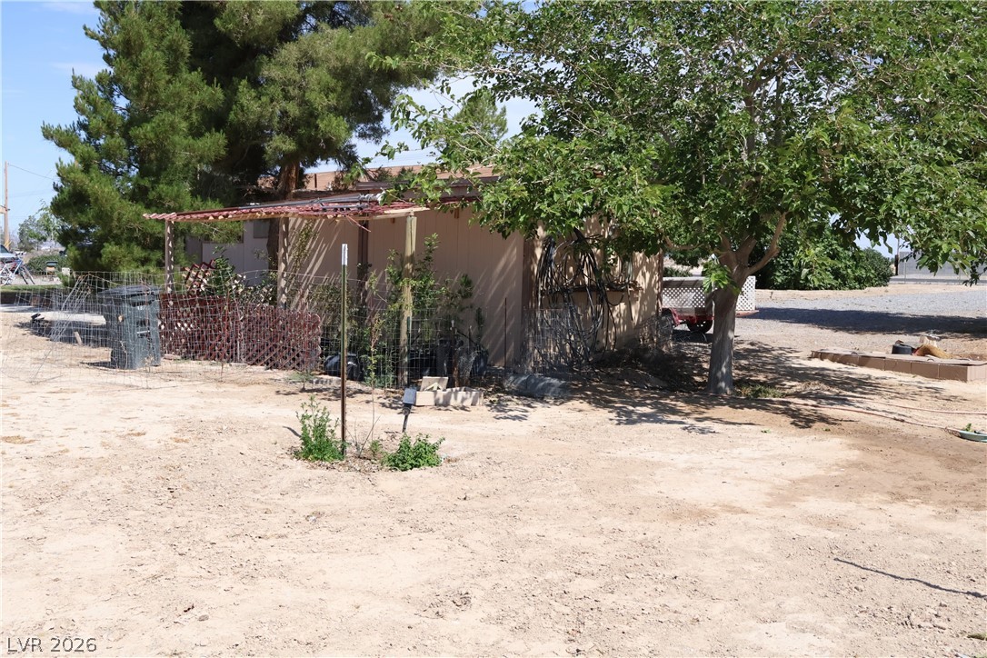 4501 East Kellogg Road Pahrump, NV 89061 - Photo 37 of 52 A well-maintained structure featuring a covered porch and mature trees, nestled within a spacious, arid landscape.