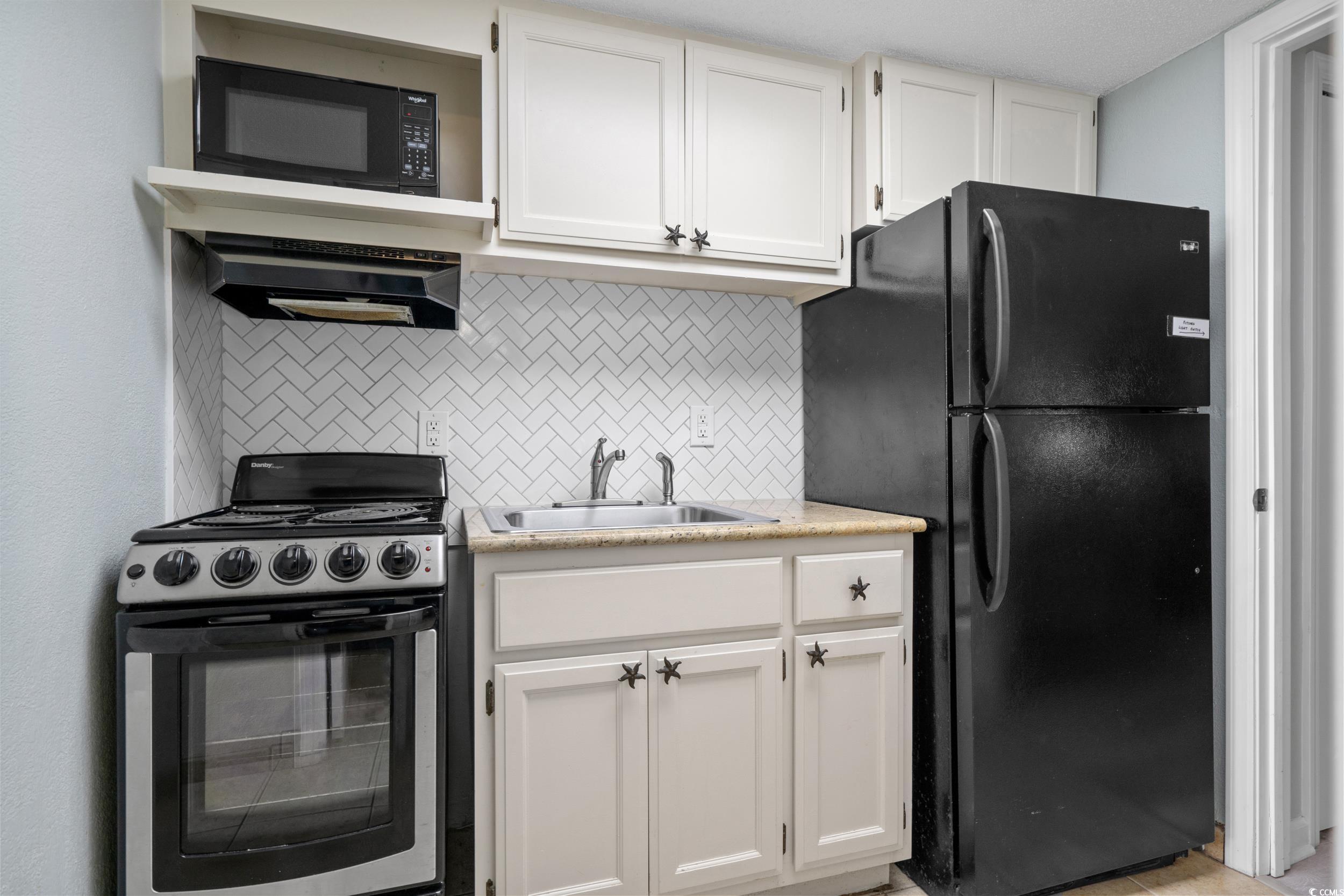 2401 South Ocean Boulevard, Unit 659 Myrtle Beach, SC 29577 - Photo 11 of 38 Kitchen with stainless steel range with electric stovetop, freestanding refrigerator, white cabinets, and decorative backsplash