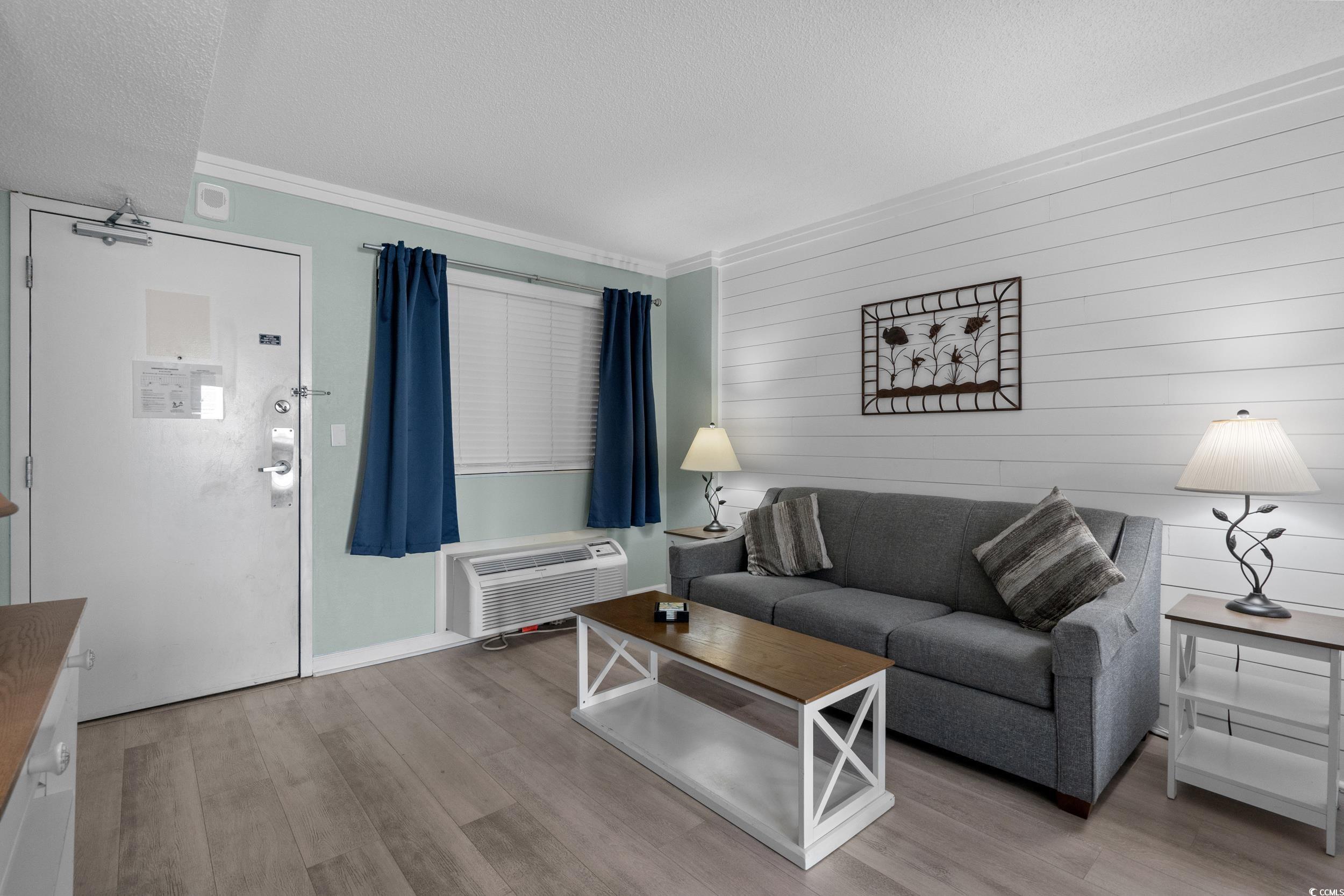 2401 South Ocean Boulevard, Unit 659 Myrtle Beach, SC 29577 - Photo 5 of 38 Living room featuring light wood finished floors, ornamental molding, wooden walls, a wall unit AC, and a textured ceiling