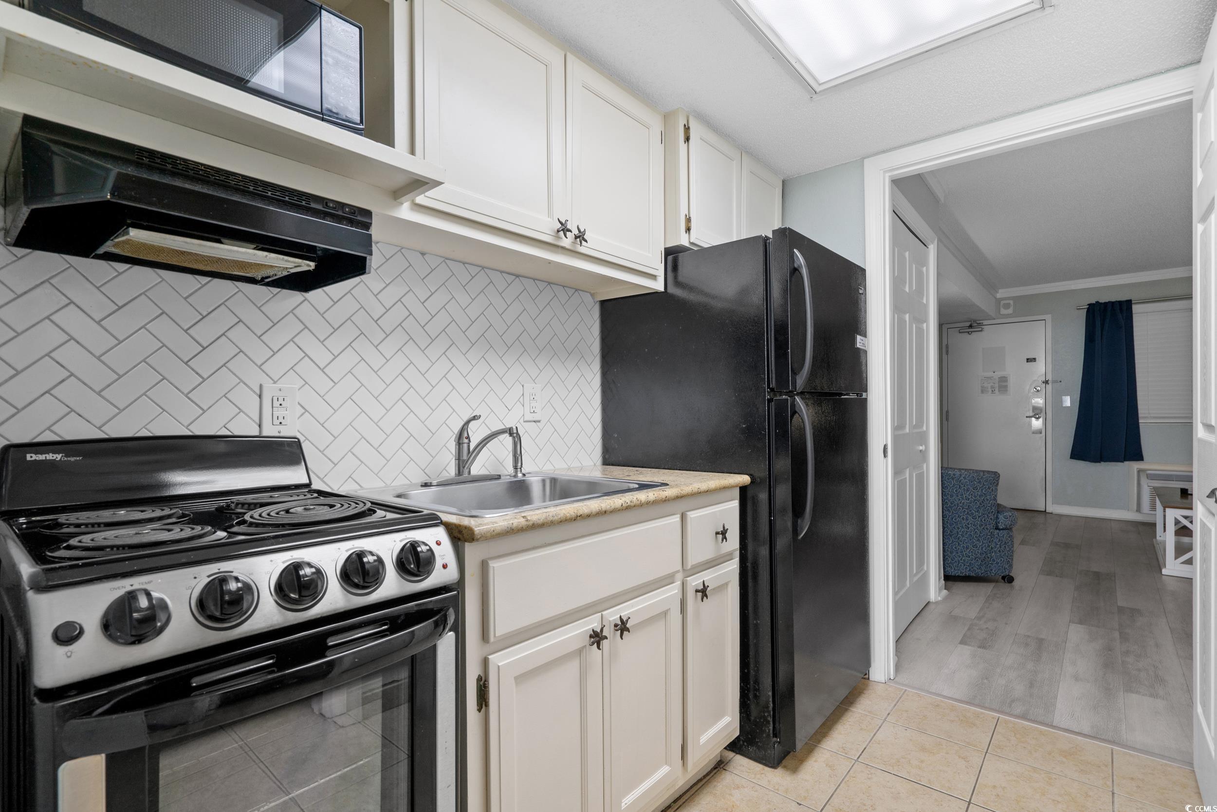 2401 South Ocean Boulevard, Unit 659 Myrtle Beach, SC 29577 - Photo 10 of 38 Kitchen with black appliances, white cabinetry, light countertops, tasteful backsplash, and exhaust hood