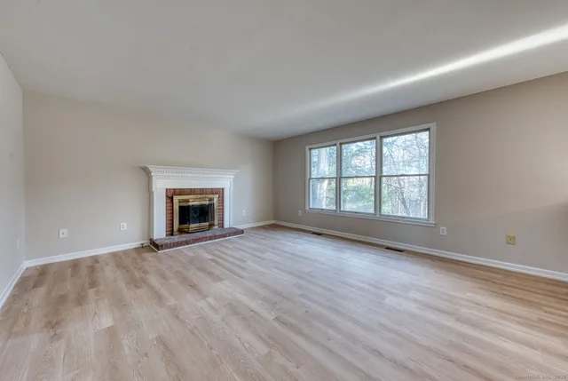 an empty room with wooden floor fireplace and windows