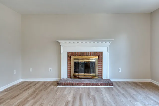 a view of an empty room with wooden floor a fireplace and a window