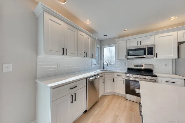 a kitchen with white cabinets appliances a sink and a window