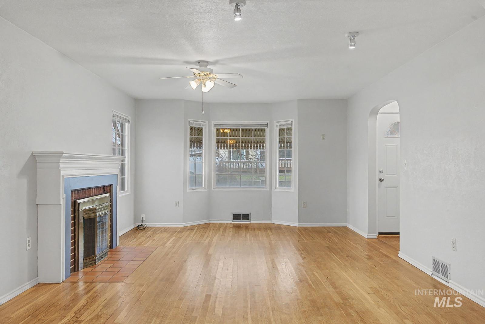 918 Elm Street Clarkston, WA 99403 - Photo 5 of 35 Unfurnished living room featuring arched walkways, a ceiling fan, light wood-type flooring, and a tile fireplace