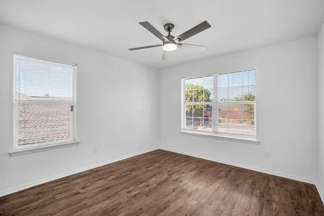 an empty room with wooden floor chandelier fan and windows
