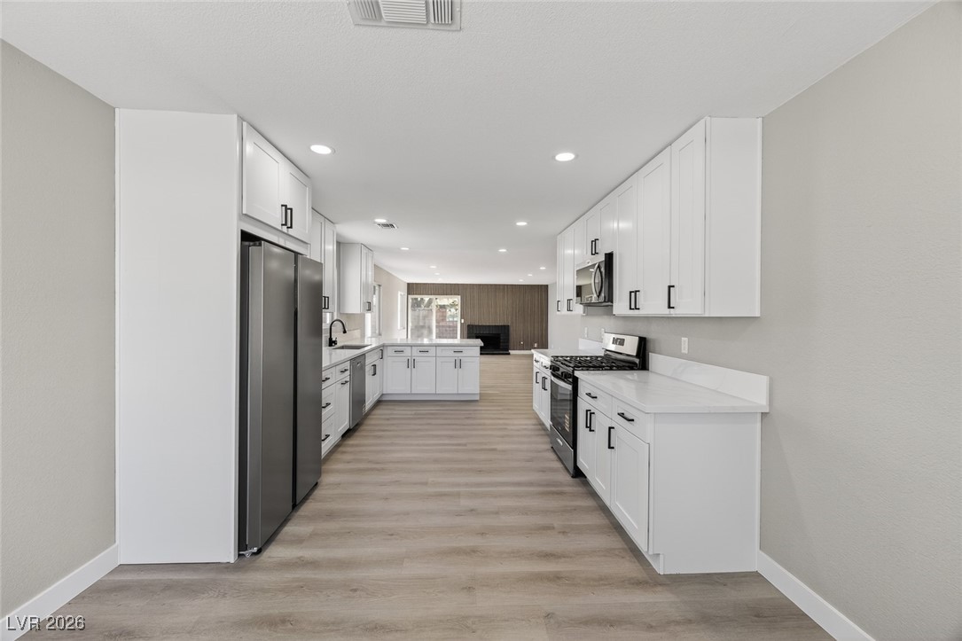 7071 Wedgewood Way Las Vegas, NV 89147 - Photo 12 of 37 Kitchen featuring white cabinets, stainless steel appliances, light wood-type flooring, a peninsula, and recessed lighting