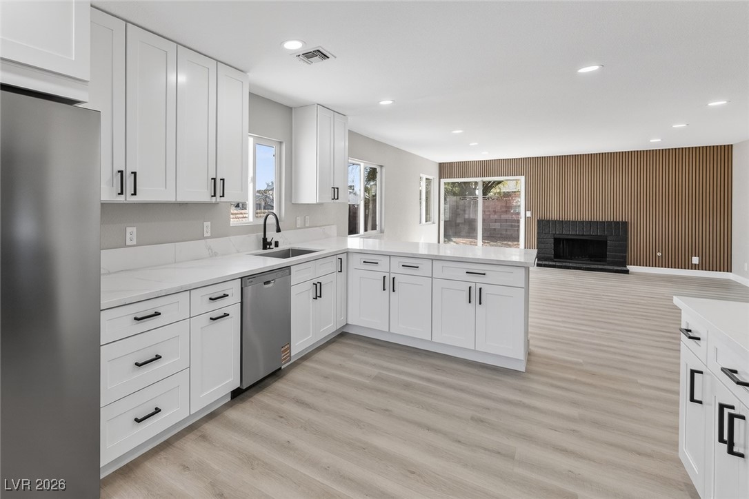 7071 Wedgewood Way Las Vegas, NV 89147 - Photo 14 of 37 Kitchen featuring stainless steel appliances, white cabinets, a peninsula, a fireplace, and light wood finished floors