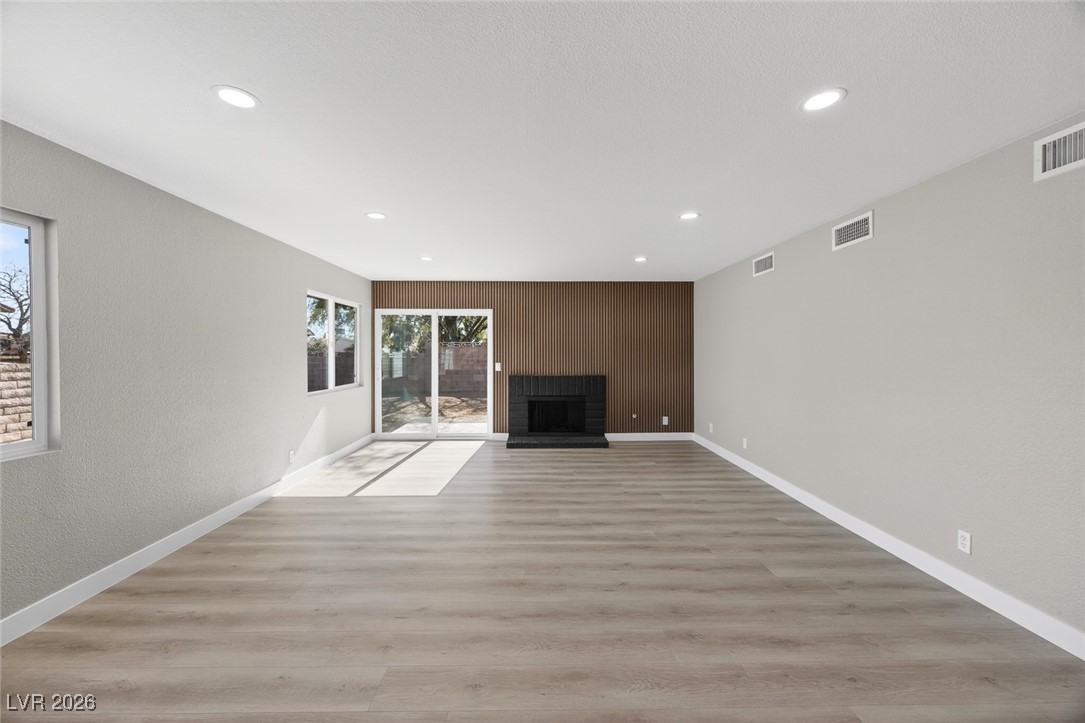 7071 Wedgewood Way Las Vegas, NV 89147 - Photo 18 of 37 Unfurnished living room featuring light wood-style flooring, a brick fireplace, a textured wall, and recessed lighting