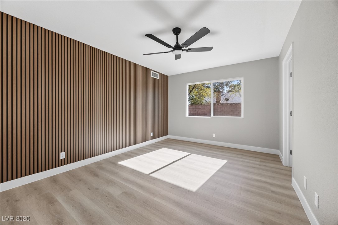 7071 Wedgewood Way Las Vegas, NV 89147 - Photo 20 of 37 Unfurnished room featuring wood walls, light wood-style floors, a ceiling fan, and an accent wall