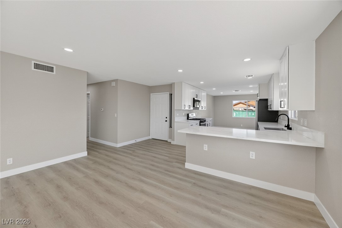 7071 Wedgewood Way Las Vegas, NV 89147 - Photo 7 of 37 Kitchen with white cabinets, stainless steel gas range oven, light wood-type flooring, light stone counters, and recessed lighting