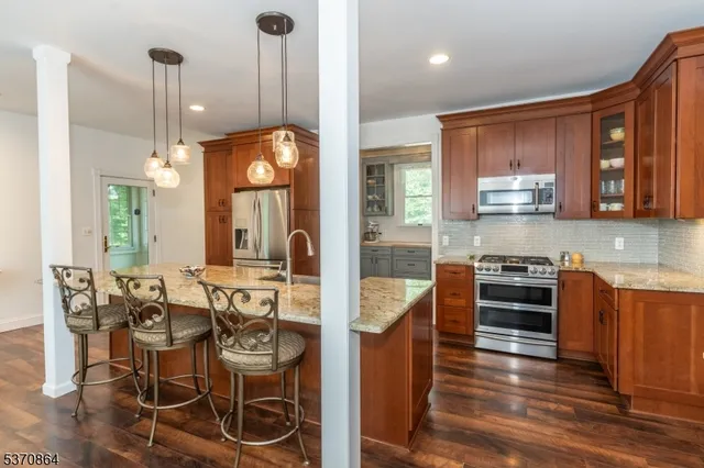 a kitchen with stainless steel appliances granite countertop a stove top oven a sink a dining table and chairs with wooden floor