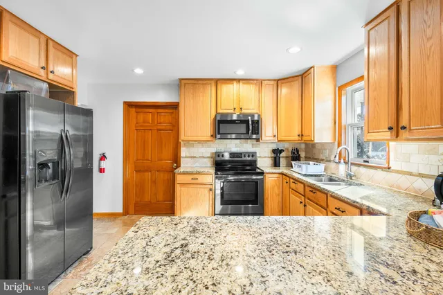 a kitchen with stainless steel appliances kitchen island granite countertop a refrigerator a stove and a sink with wooden floor