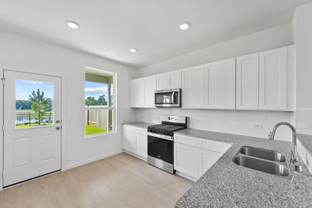 a kitchen with stainless steel appliances granite countertop a sink a stove a refrigerator a window with white cabinets and wooden floor