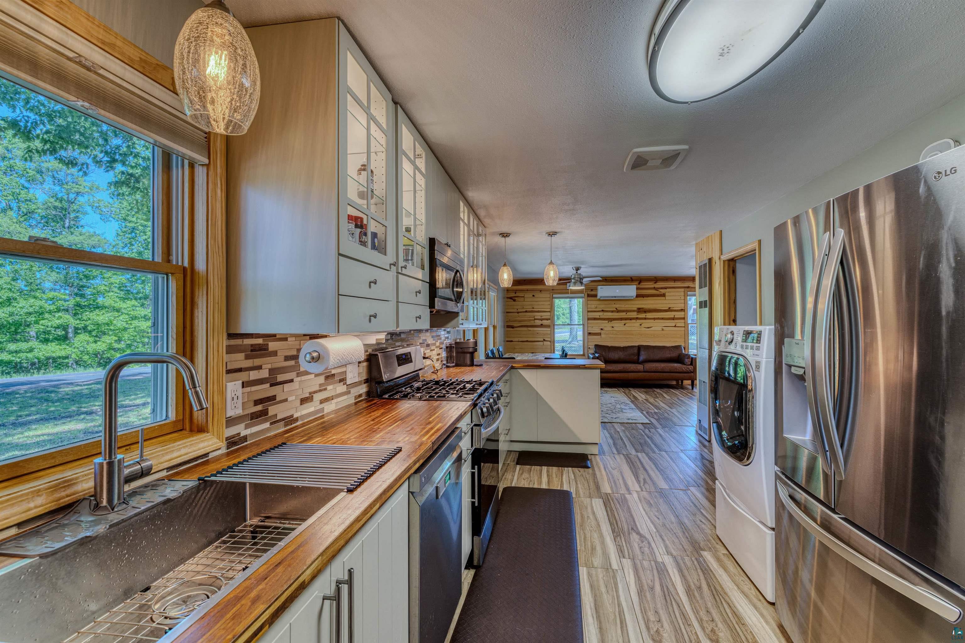 66075 Rooster Road Iron River, WI 54847 - Photo 26 of 52 Kitchen featuring wood-finish countertops, stainless steel appliances, a tile backsplash, and overhead cabinetry with glass-front doors