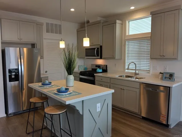 a kitchen with stainless steel appliances kitchen island granite countertop a dining table chairs sink refrigerator and microwave