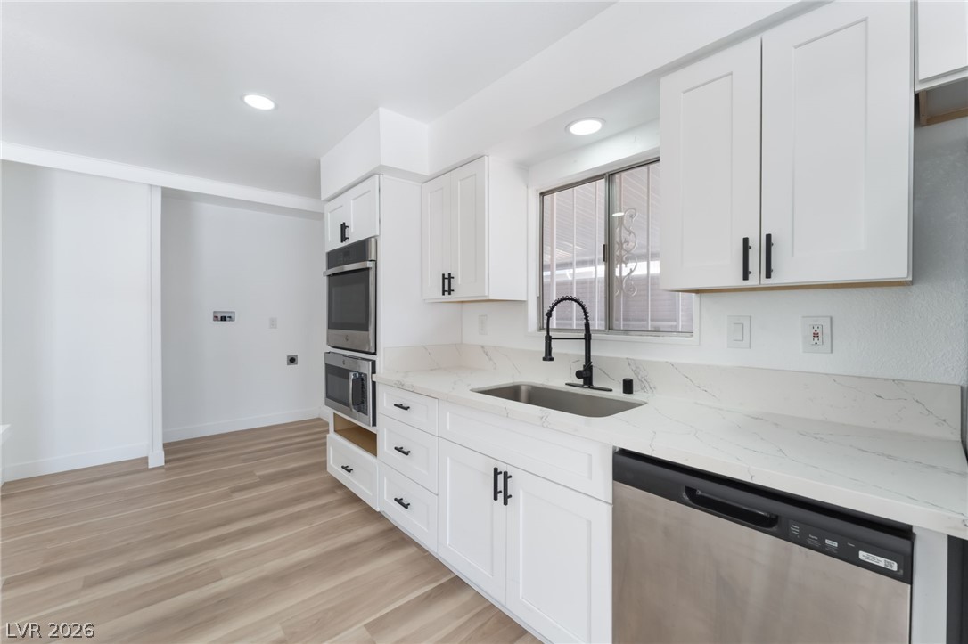 4980 Ridge Drive Las Vegas, NV 89103 - Photo 2 of 36 Kitchen with light stone counters, stainless steel appliances, white cabinets, light wood-style floors, and recessed lighting