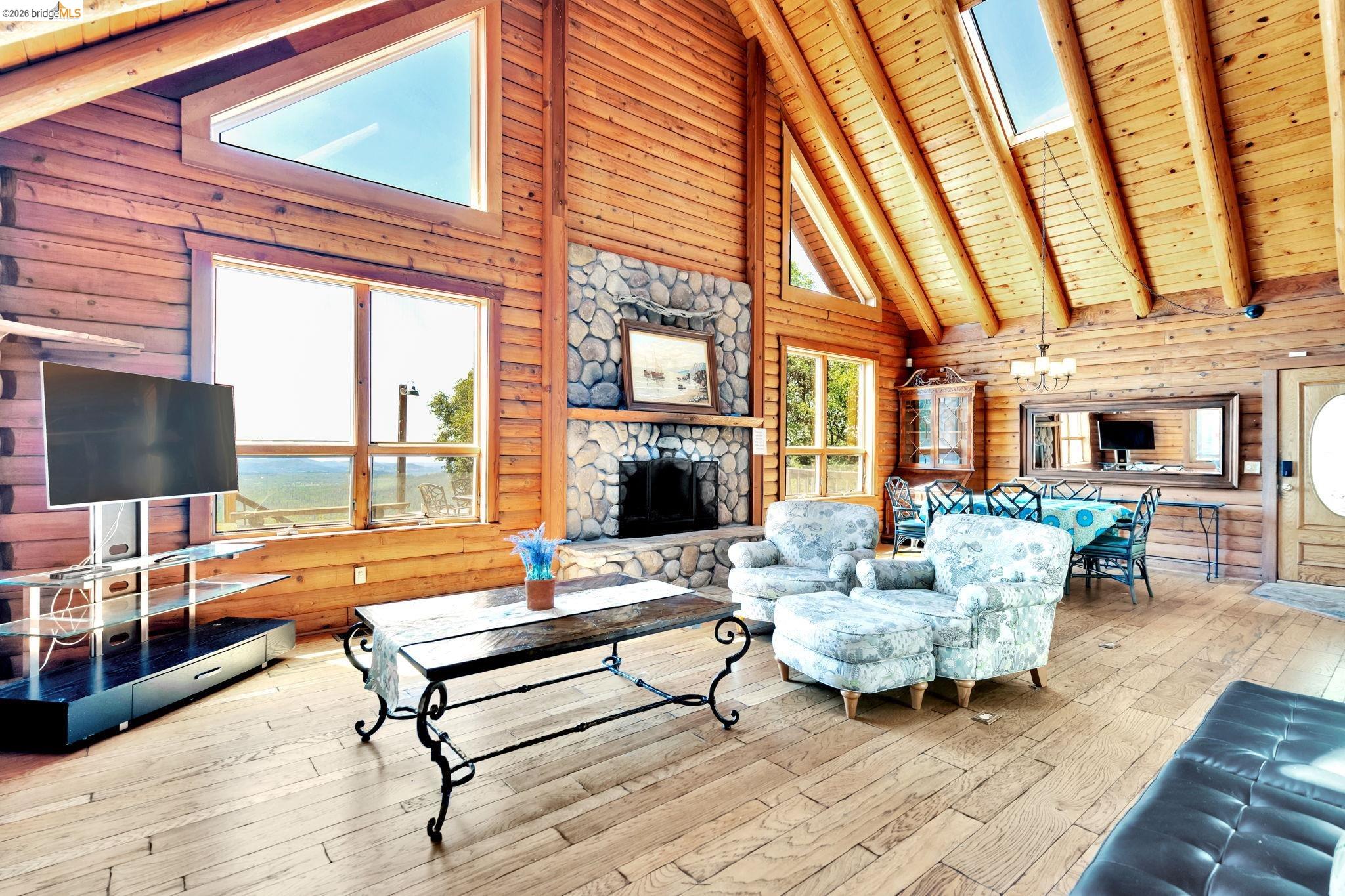 14799 Big Hill Road Sonora, CA 95370 - Photo 11 of 60 Living area featuring a skylight, a high wooden beamed ceiling, hardwood / wood-style floors, a chandelier, and a fireplace