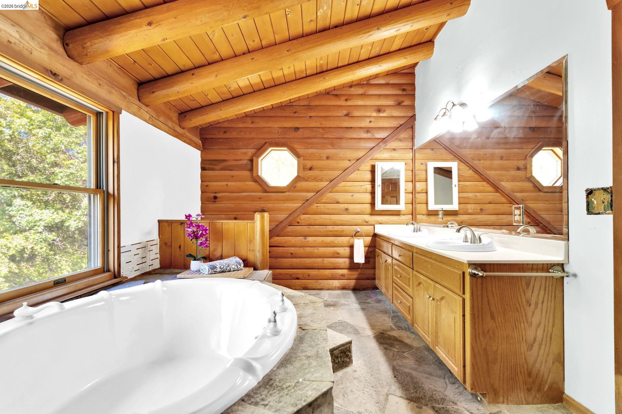 14799 Big Hill Road Sonora, CA 95370 - Photo 32 of 60 Full bath with log walls, double vanity, a bath, a wooden ceiling with exposed beams, and light stone finish floors