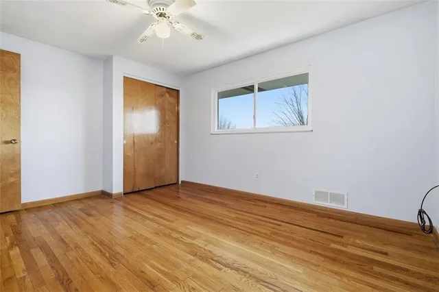 a view of an empty room with wooden floor and a ceiling fan