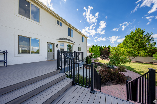 868 Braddock Lane Alpine, UT 84004 - Photo 23 of 64 Expansive composite deck with black metal railings, offering direct access to a landscaped backyard featuring mature trees, a manicured lawn, and a stamped concrete pathway
