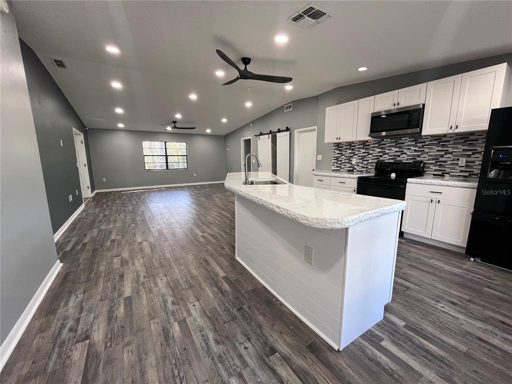 8122 Matthew Drive New Port Richey, FL 34653 - Photo 4 of 25 a large white kitchen with kitchen island a stove a sink dishwasher a microwave oven and a dining table with wooden floor