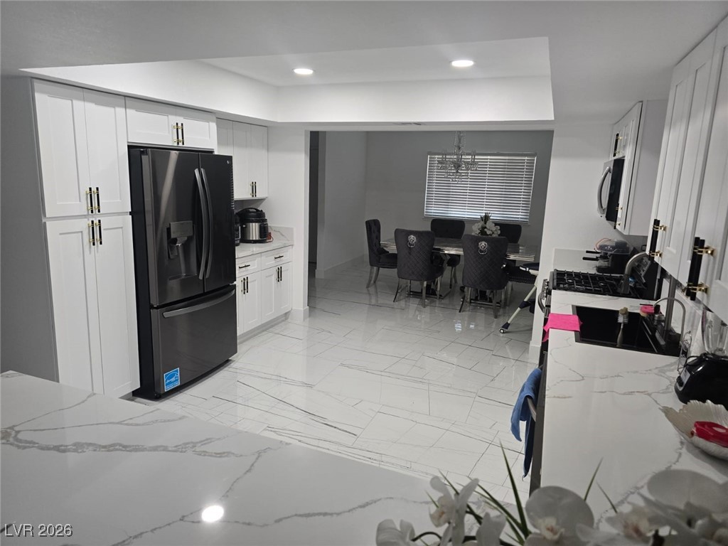 3153 Downing Place Las Vegas, NV 89121 - Photo 4 of 7 Kitchen with light stone countertops, black fridge with ice dispenser, white cabinetry, recessed lighting, and light marble finish floors