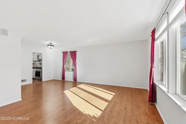an empty room with wooden floor fan and windows