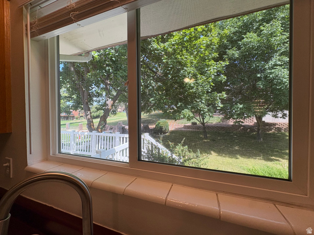 595 Meadowlark Road Orem, UT 84097 - Photo 20 of 87 Kitchen window featuring a tiled sill, stainless steel faucet, and a backyard landscape with mature trees and a white railing