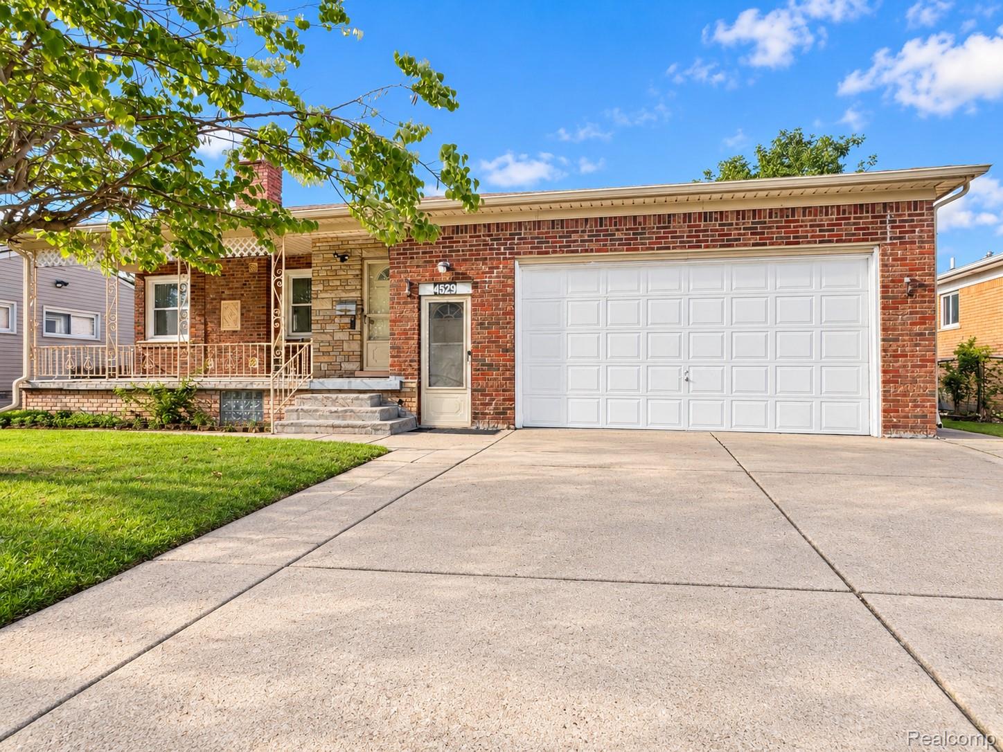 4529 Frazho Road Warren, MI 48091 - Photo 2 of 9 Brick and stone facade, covered front porch with decorative railing, expansive concrete driveway, attached garage with paneled door, and a manicured front lawn