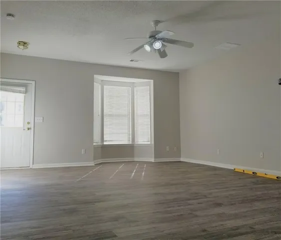 a view of an empty room with wooden floor and fan
