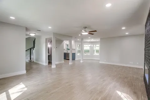 a view of an empty room with wooden floor and a kitchen