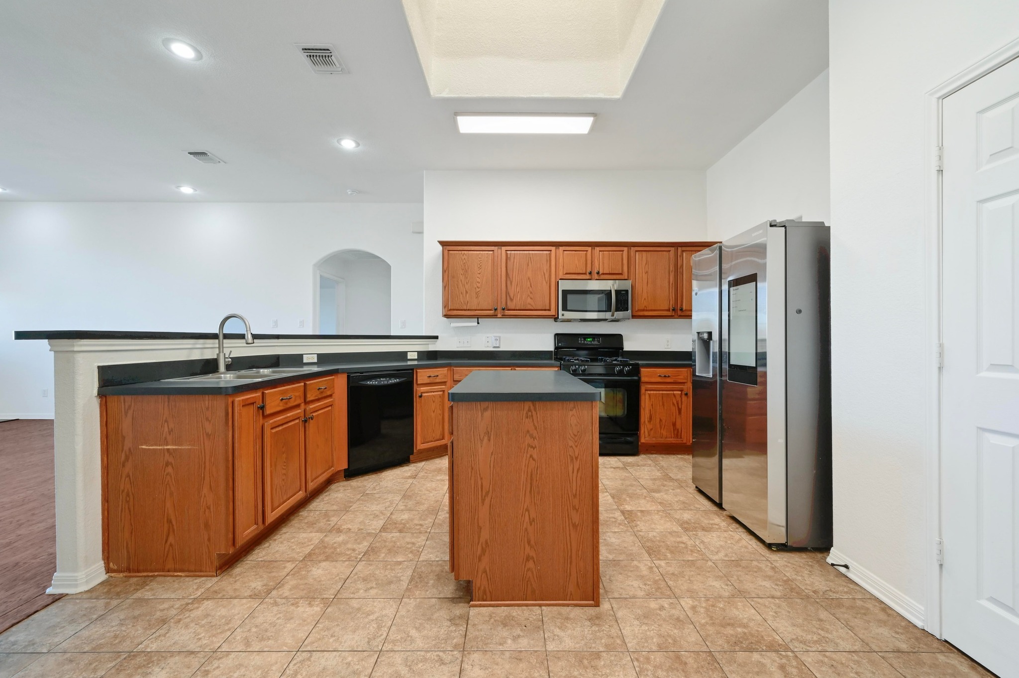 198 Valruth Drive Kyle, TX 78640 - Photo 17 of 32 Kitchen with brown cabinets, dark countertops, black appliances, a kitchen island, and arched walkways