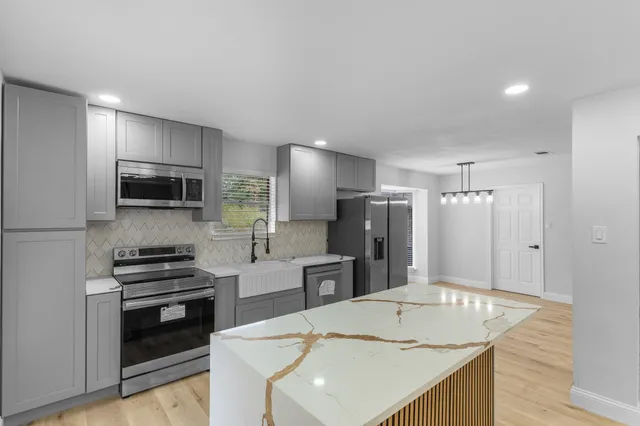 a view of an empty room and kitchen with wooden floor