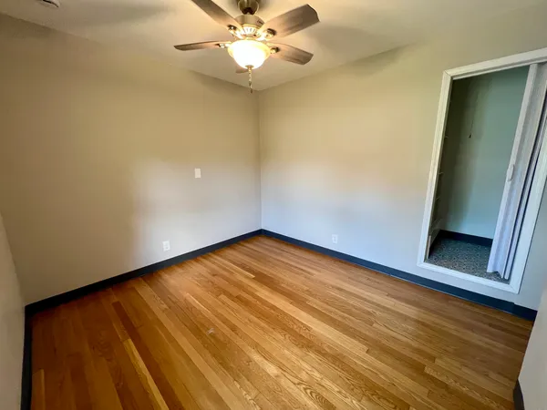 an empty room with wooden floor and fan