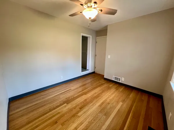 a view of an empty room with wooden floor and a ceiling fan